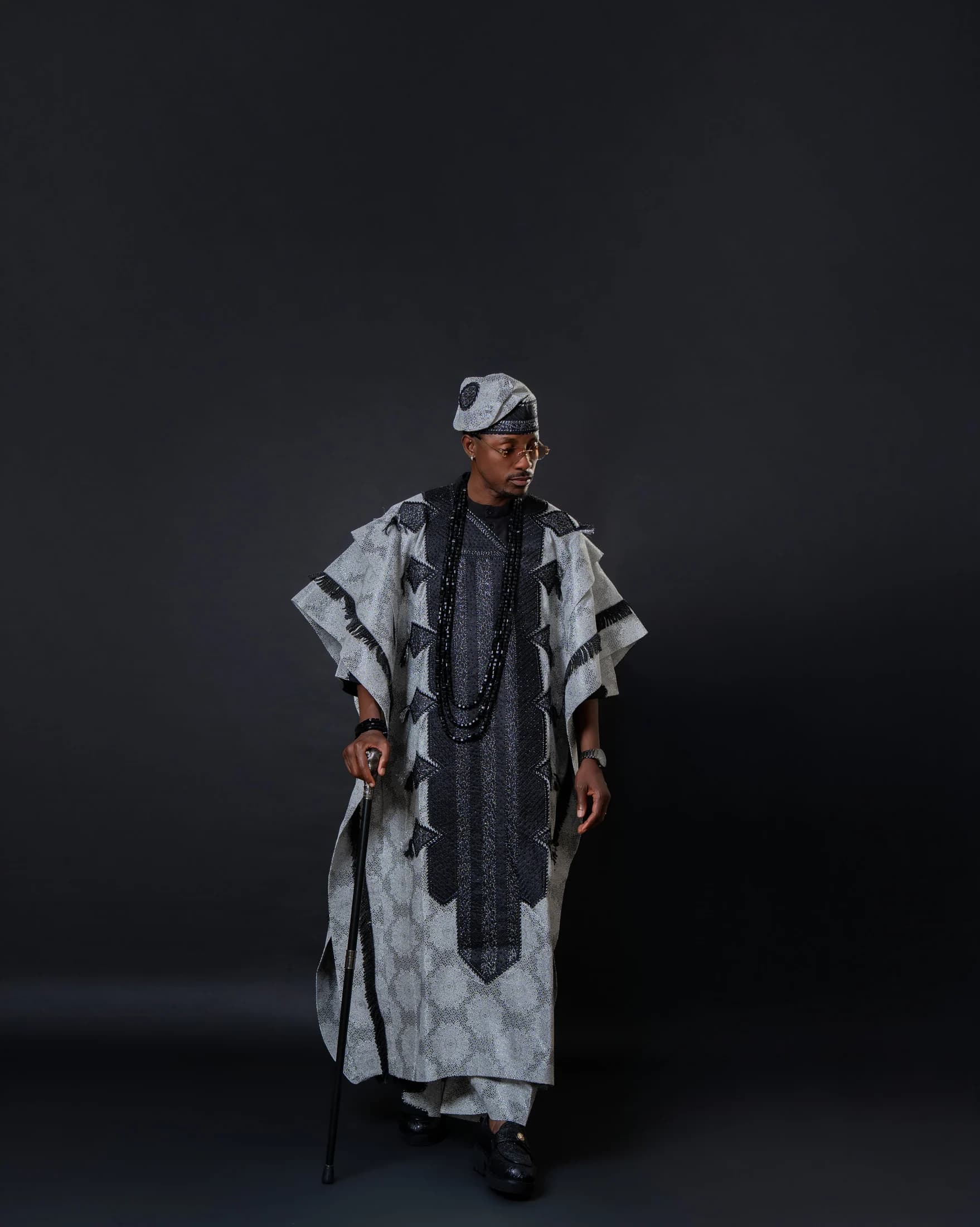Full-length portrait of Philip Akinjobi looking down while holding a ceremonial walking stick