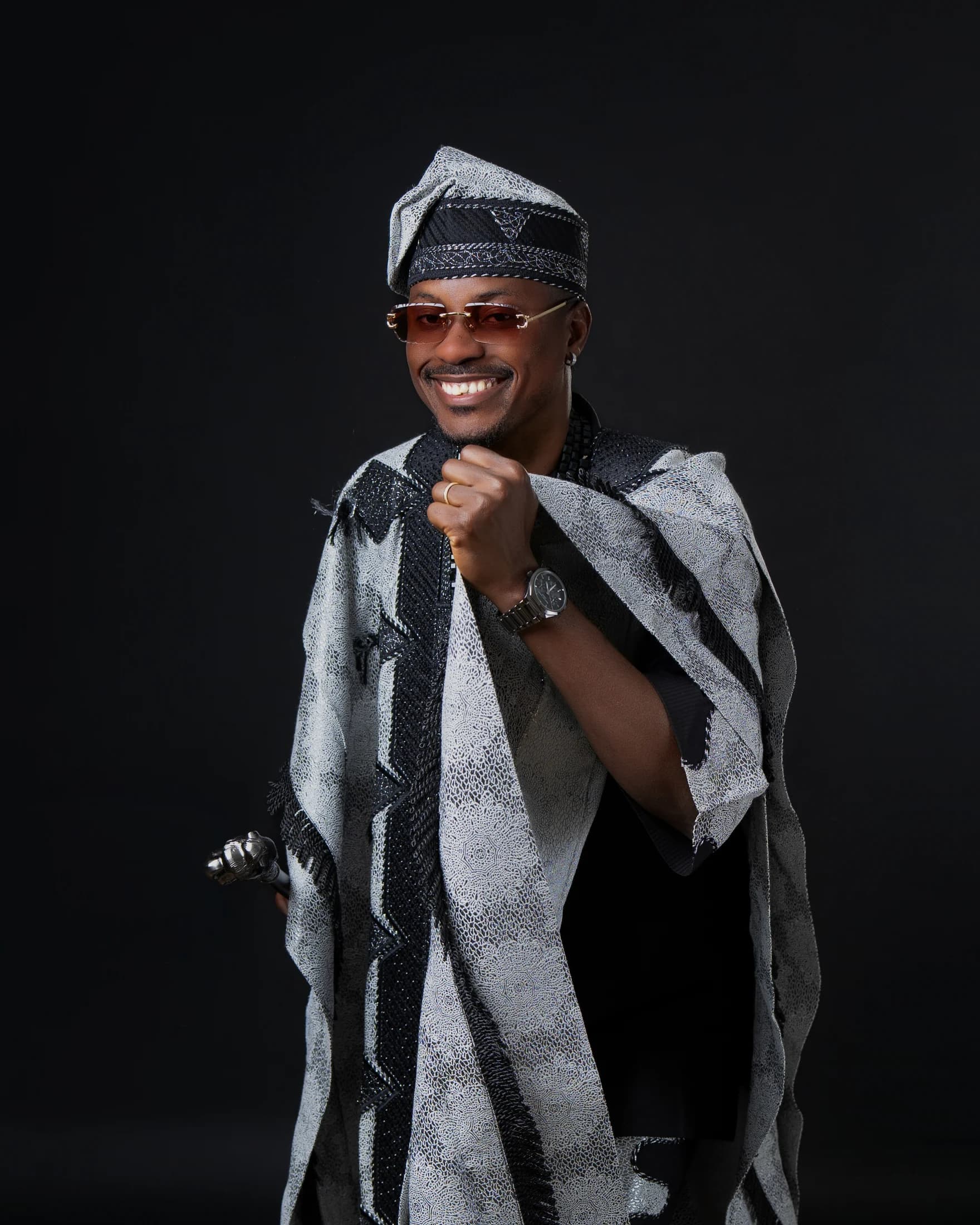 Philip Akinjobi smiling in a close portrait while holding his black-and-silver agbada