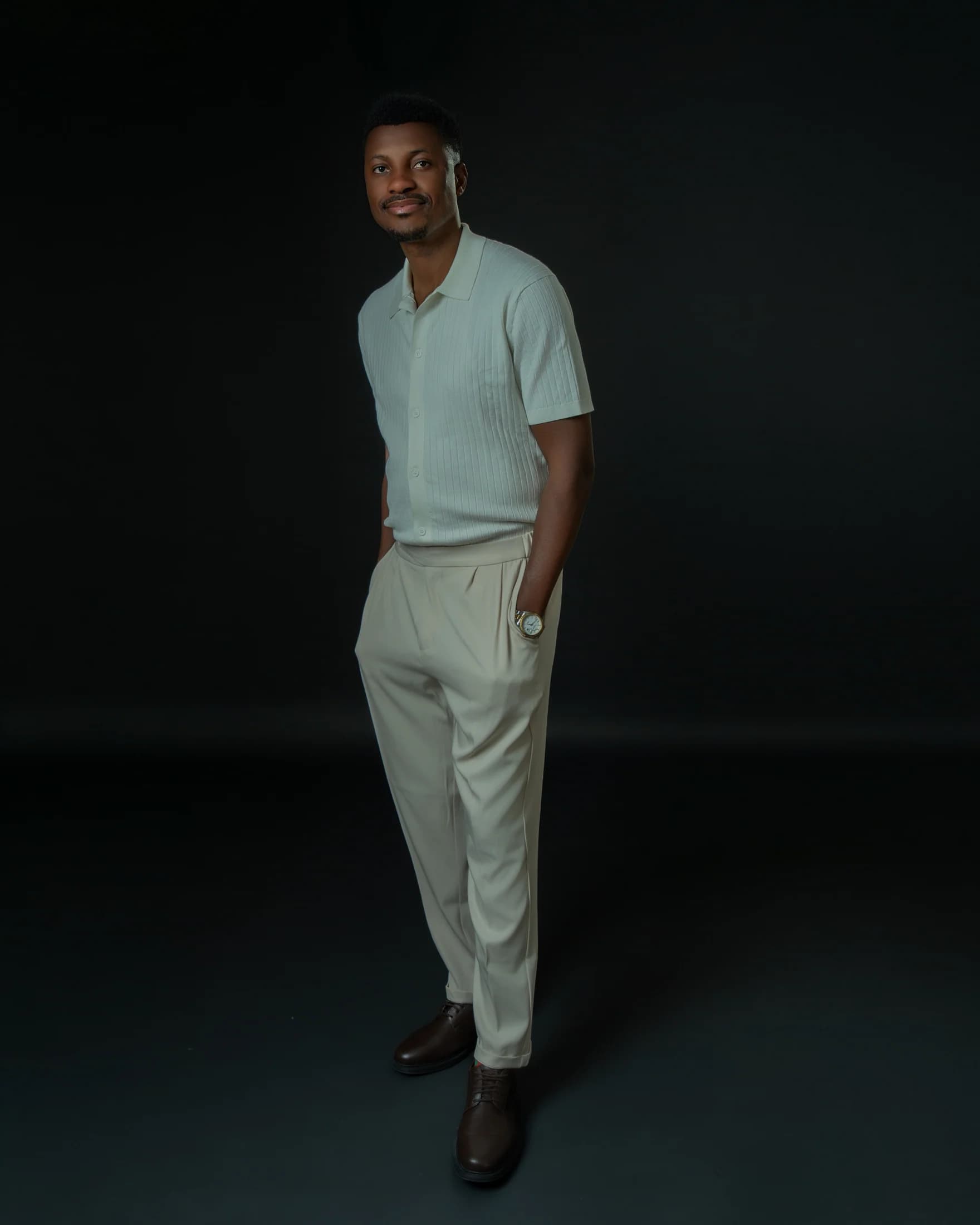 Full-length portrait of Philip Akinjobi standing in an ivory knit shirt and trousers