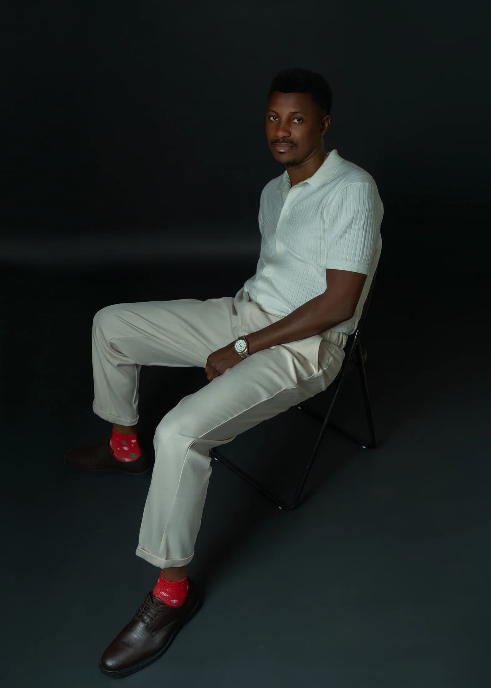 Philip Akinjobi seated in an ivory outfit with bright red patterned socks